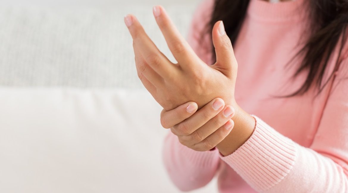 Closeup woman sitting on sofa holds her wrist hand injury, feeling pain. Health care and medical concept.